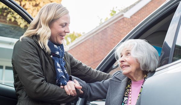 female helping older woman from a car