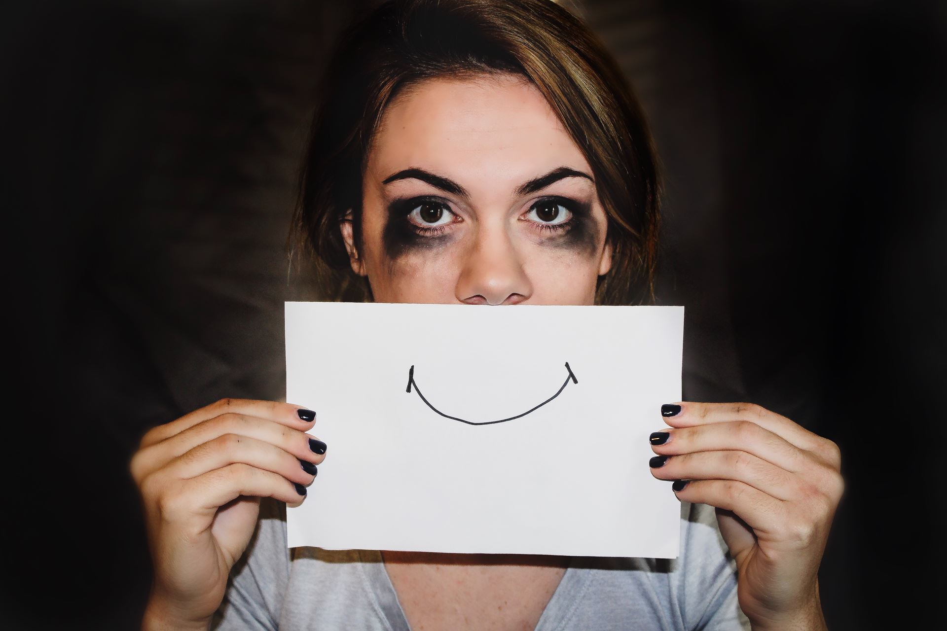 a person with smudged eyes holding a paper smile over her mouth