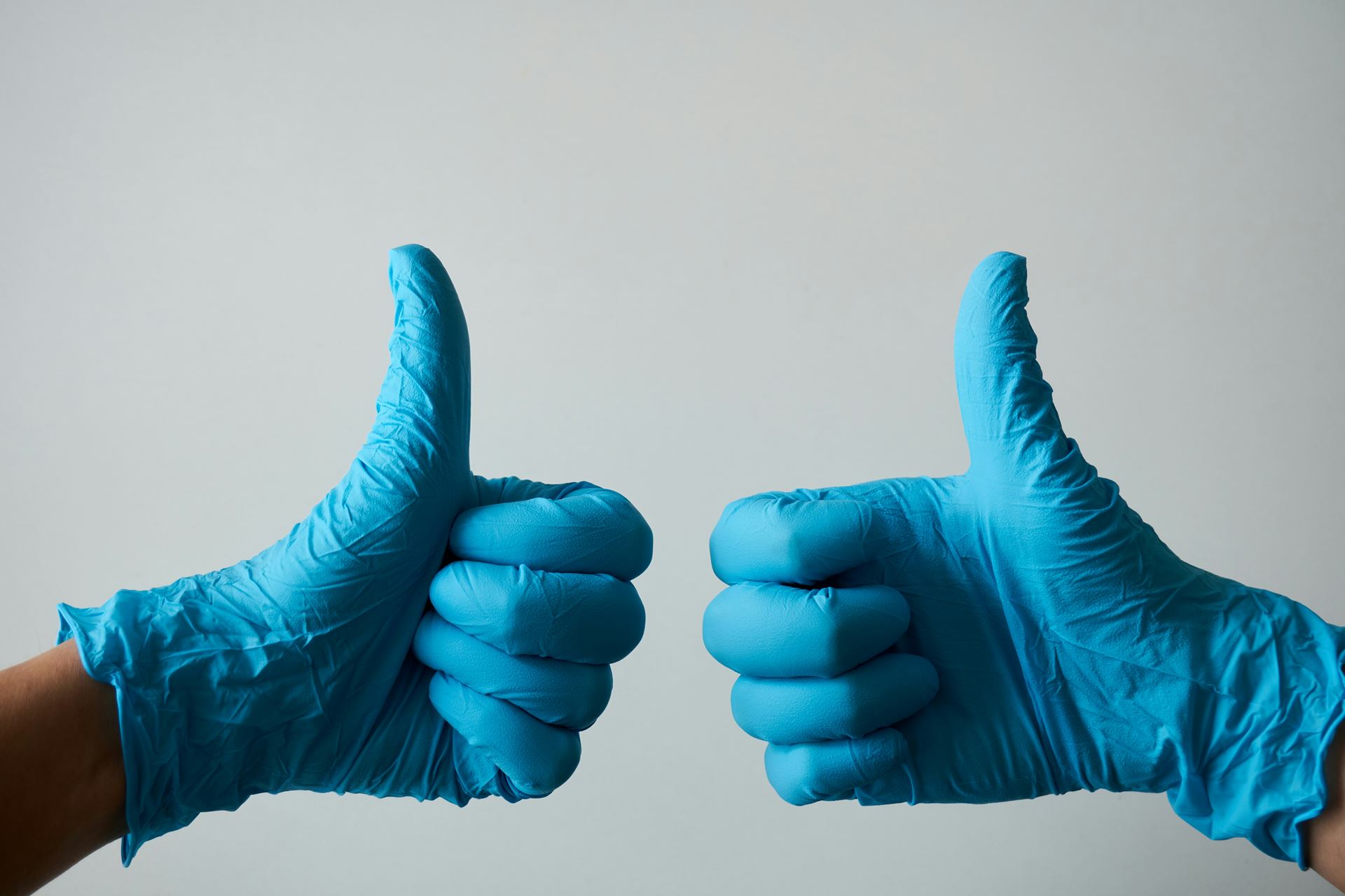 a pair of hands in medical gloves giving a thumbs up gesture